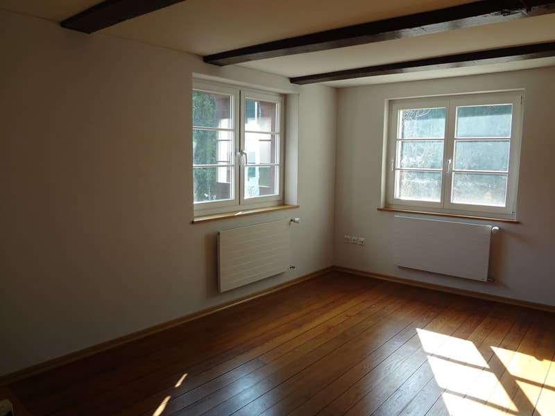 Empty room with two windows, wooden floor, two radiators, power outlets