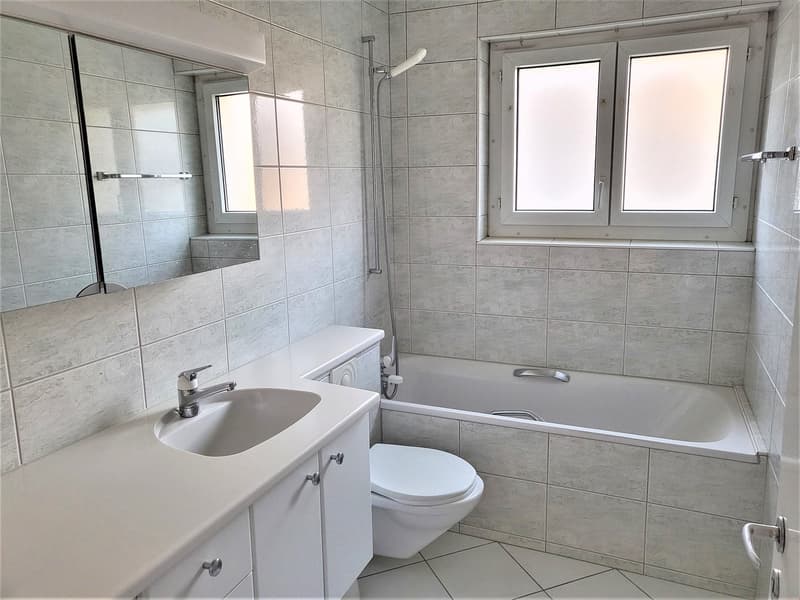 Bathroom with white tiles, bathtub, toilet, sink, mirror, and shower head