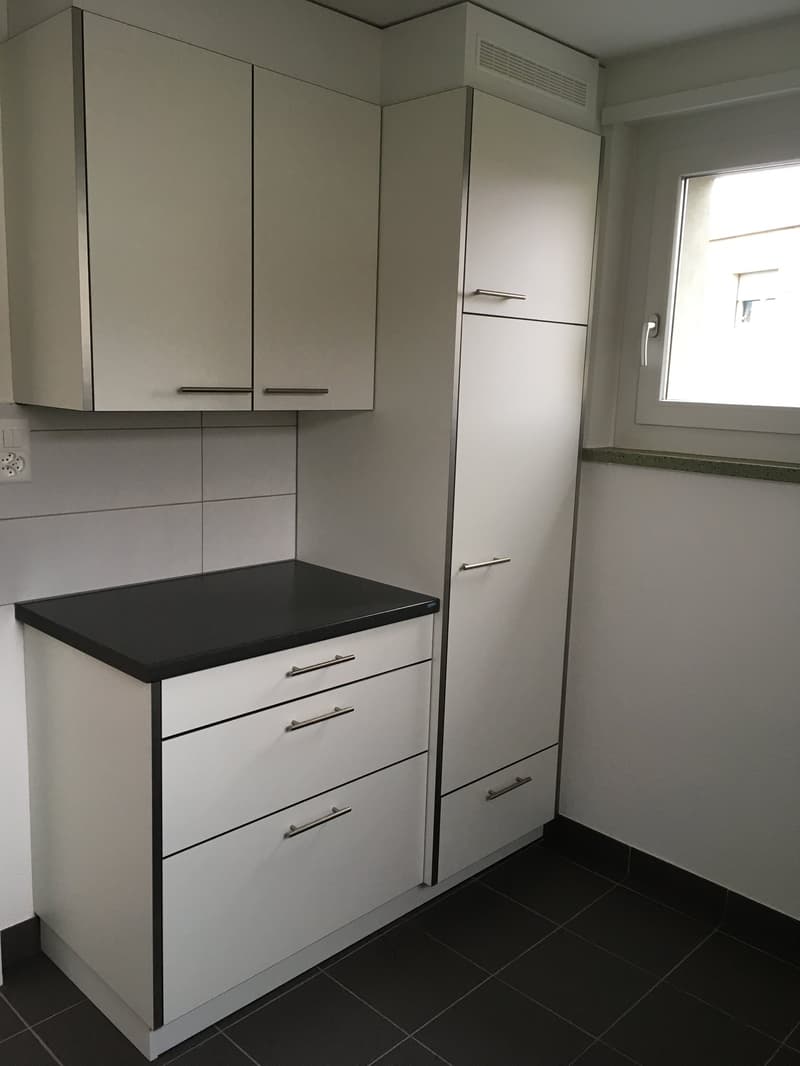 modern kitchen with white cabinets, black countertop, drawers, and a window