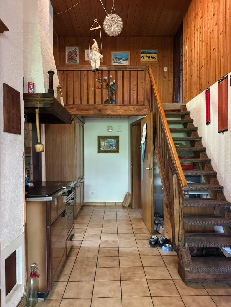 kitchen with wooden cabinets, tiled floor, wooden staircase, wooden ceiling, hanging lamp, picture frames, open door, hallway