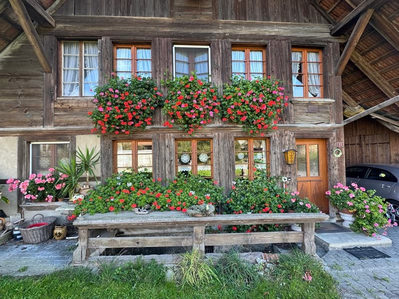 Traditional wooden house with flower boxes, wooden door, wooden bench, car parked in front