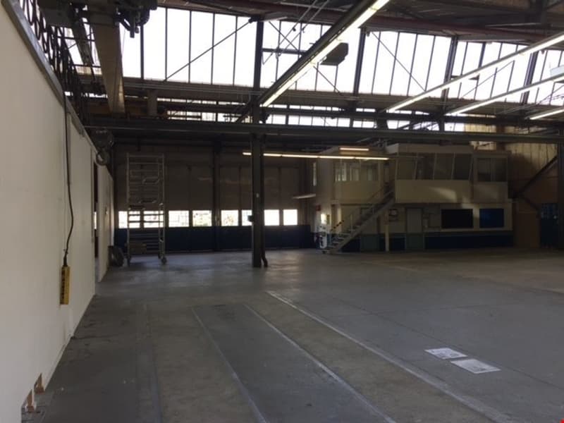 Large open warehouse space with high ceilings, concrete floor, and exposed steel beams and trusses supporting the roof structure.