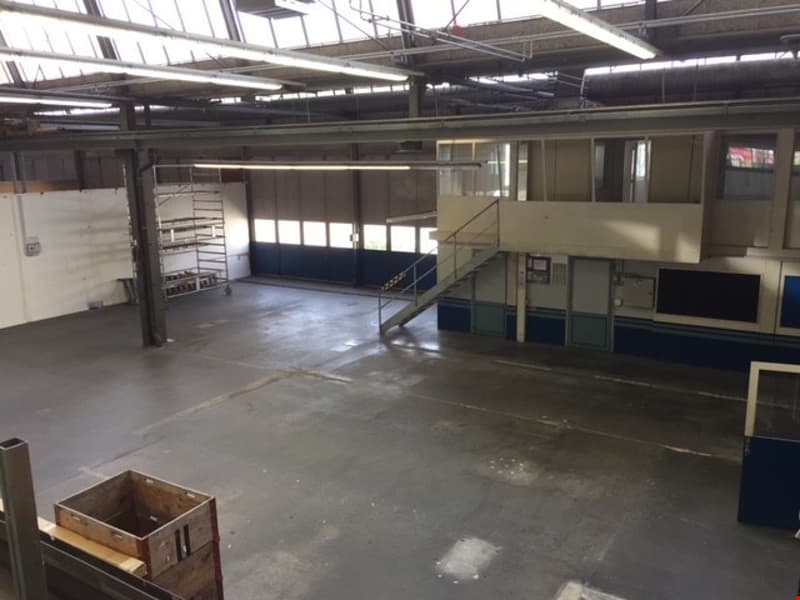 Large open space with high ceilings, concrete floor, and various storage units and equipment visible. The space appears to be a warehouse or industrial facility.