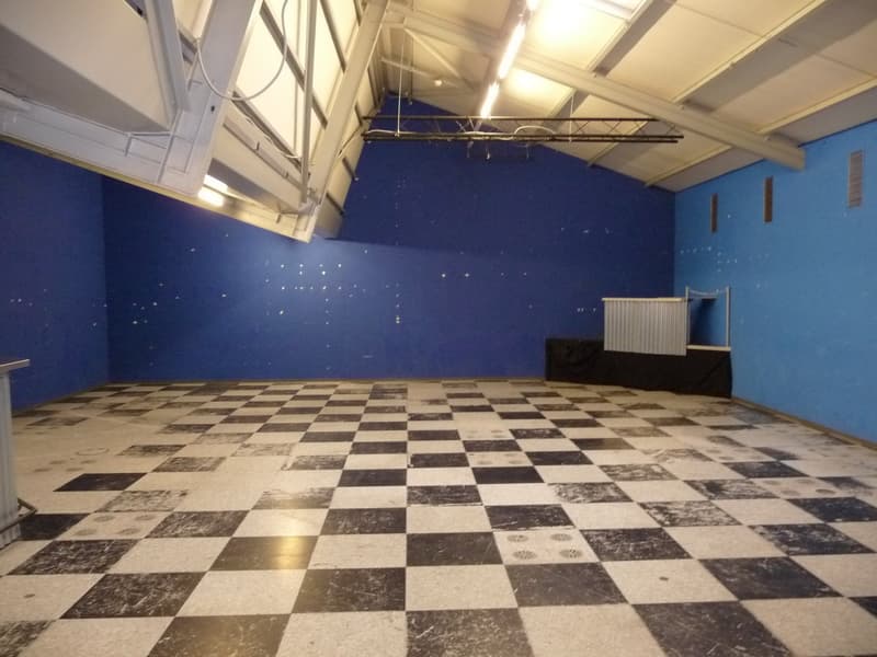 Large open space with a checkered tile floor, blue walls, and a high ceiling with exposed beams. The room appears to be a studio or workshop space.