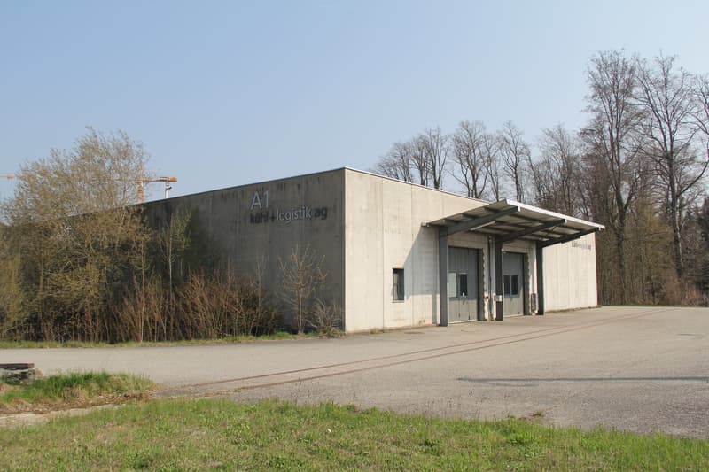 Large industrial building with concrete walls and large doors, set on a raised ground floor.