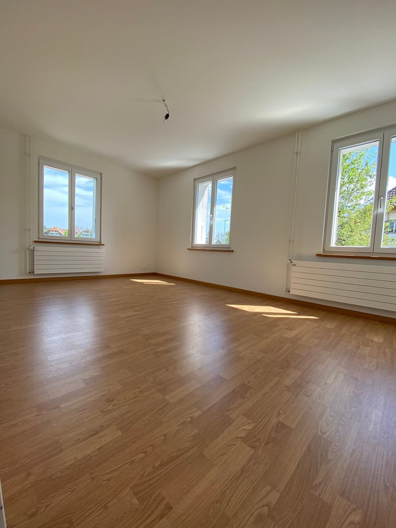 room with three windows, hardwood flooring, two radiators, bright sunlight