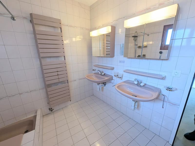 Bathroom with white tiles, two sinks, a bathtub, and two mirrors with lights