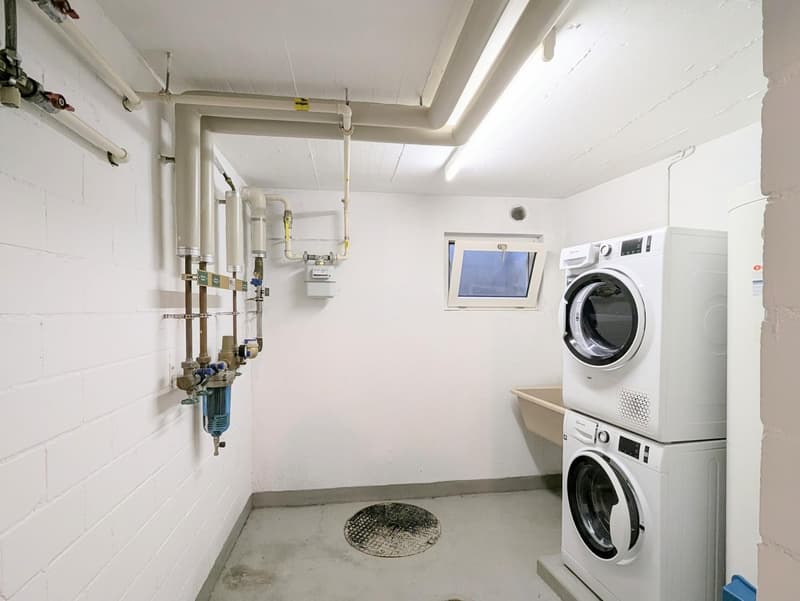 Laundry room with white walls, white ceiling, white washing machines, small window, pipes, and a sink
