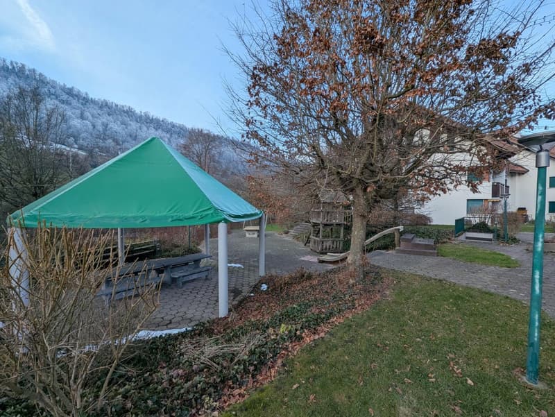 green tent, bench, tree, house, mountain in the background