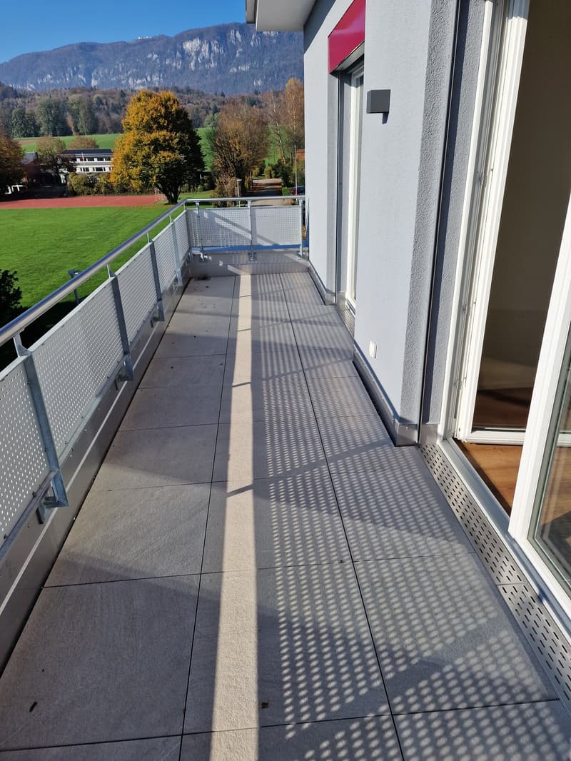 balcony with gray tiled floor and metal railings, overlooking green landscape