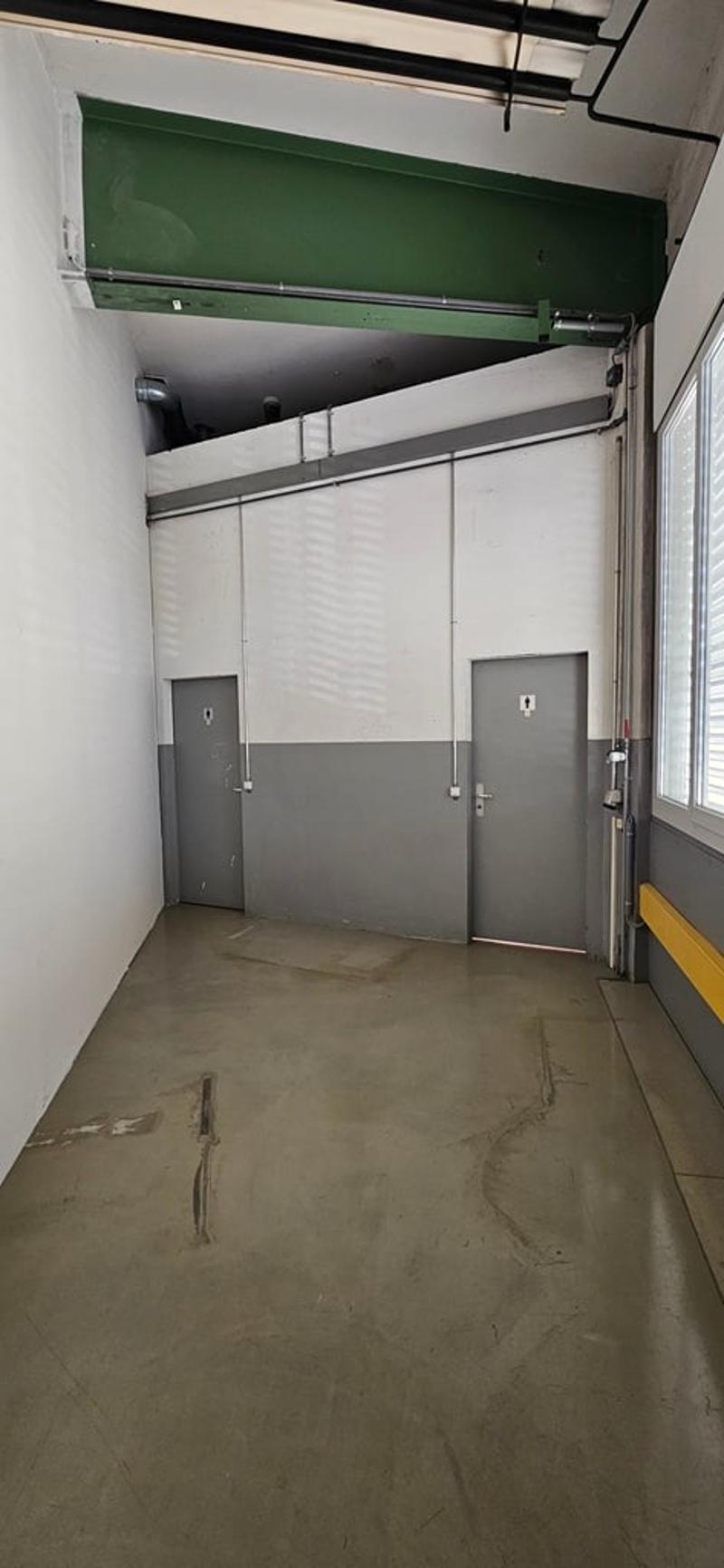 Empty parking area with two doors, concrete floor, white walls, yellow barrier