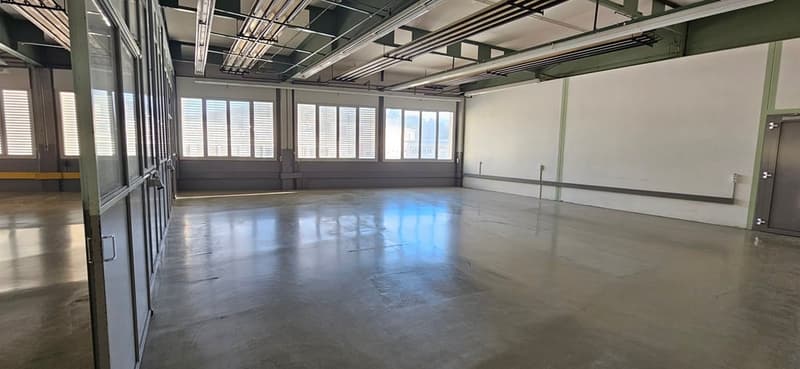 Empty room with concrete floor, large windows, metal beams, and doors