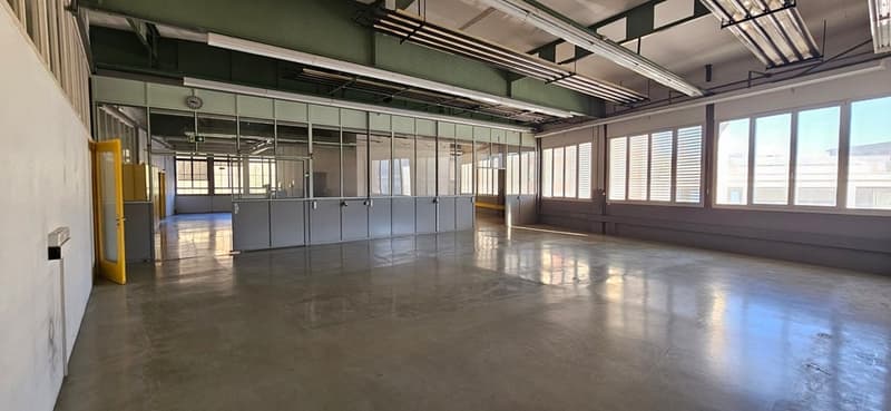 Empty room with concrete floor, glass walls, large windows, and fluorescent ceiling lights