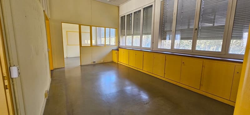 Empty room with yellow cabinets, large windows, concrete floor, and a door.