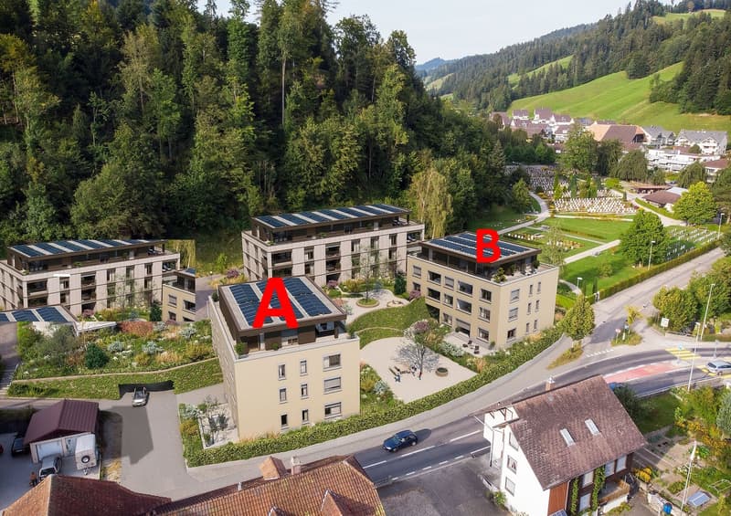 Multi-story apartment buildings with solar panels on the roofs, surrounded by green landscaping and a road. The buildings are labeled with the letters 'A' and 'B'.