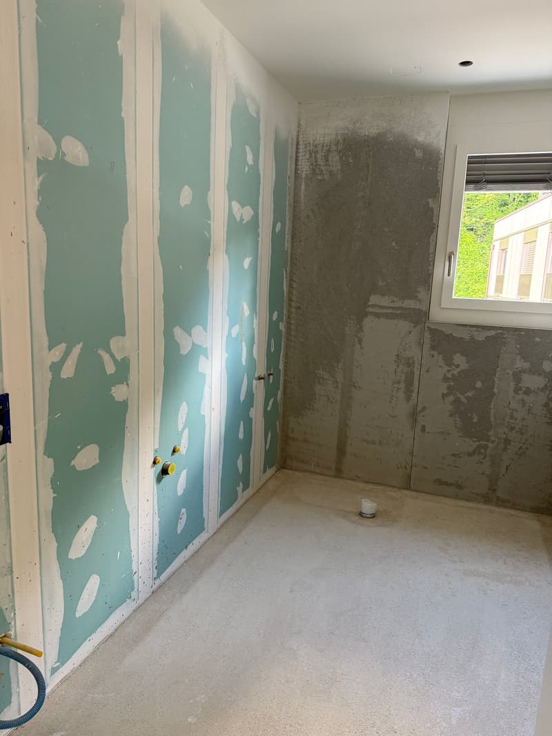 Unfinished room with drywall panels on the walls, concrete floor, and a window visible.