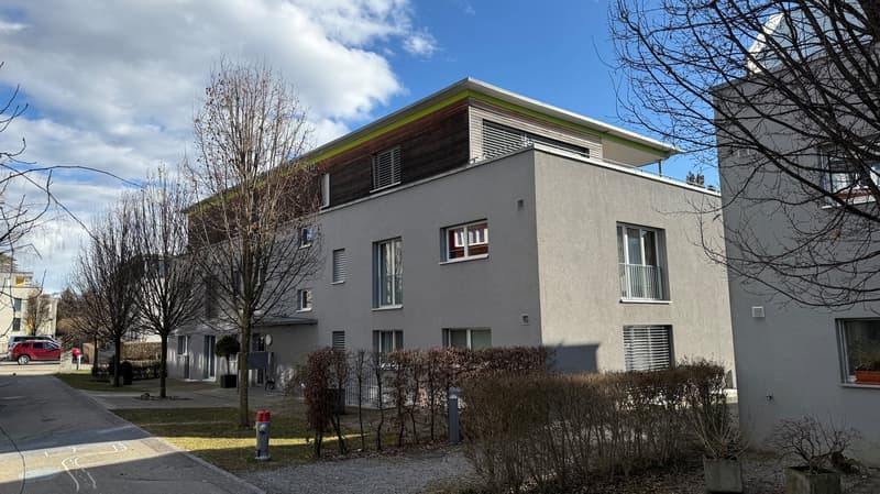 Gray building with several floors, many windows, flat roof, concrete pathway