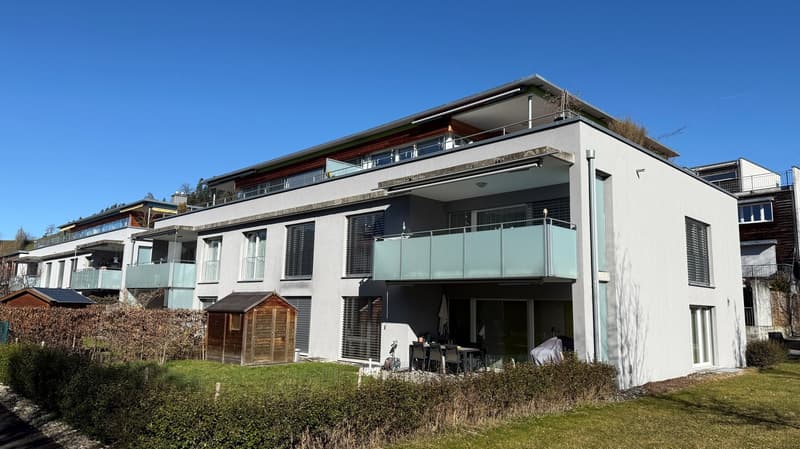 two story white house with multiple balconies, one has glass railings, solar panels on one of the houses in the background