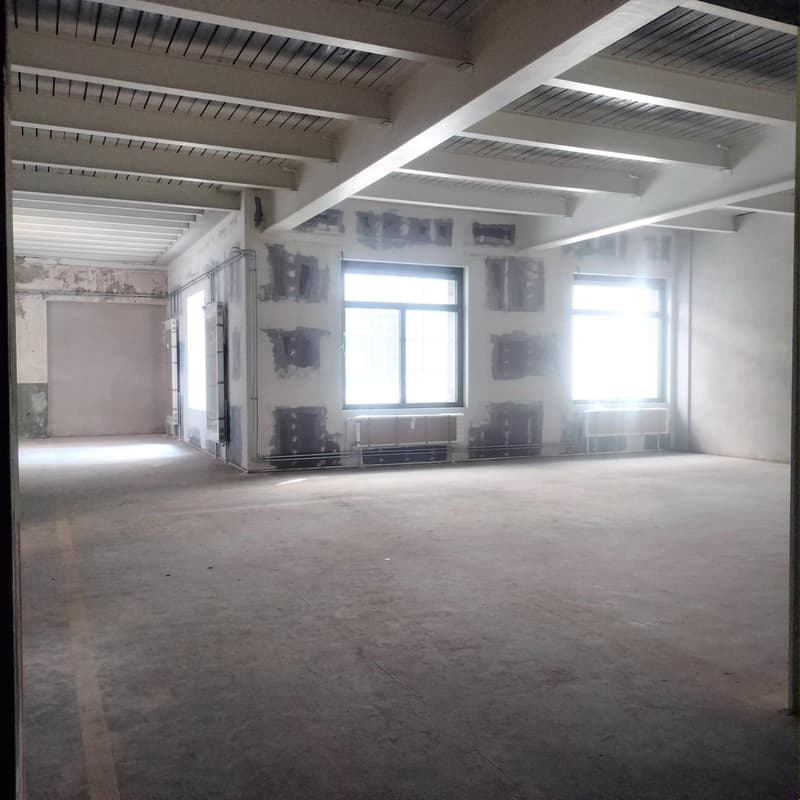empty room, unfinished walls, high ceiling, windows on opposite walls, grey floor, light coming in from windows