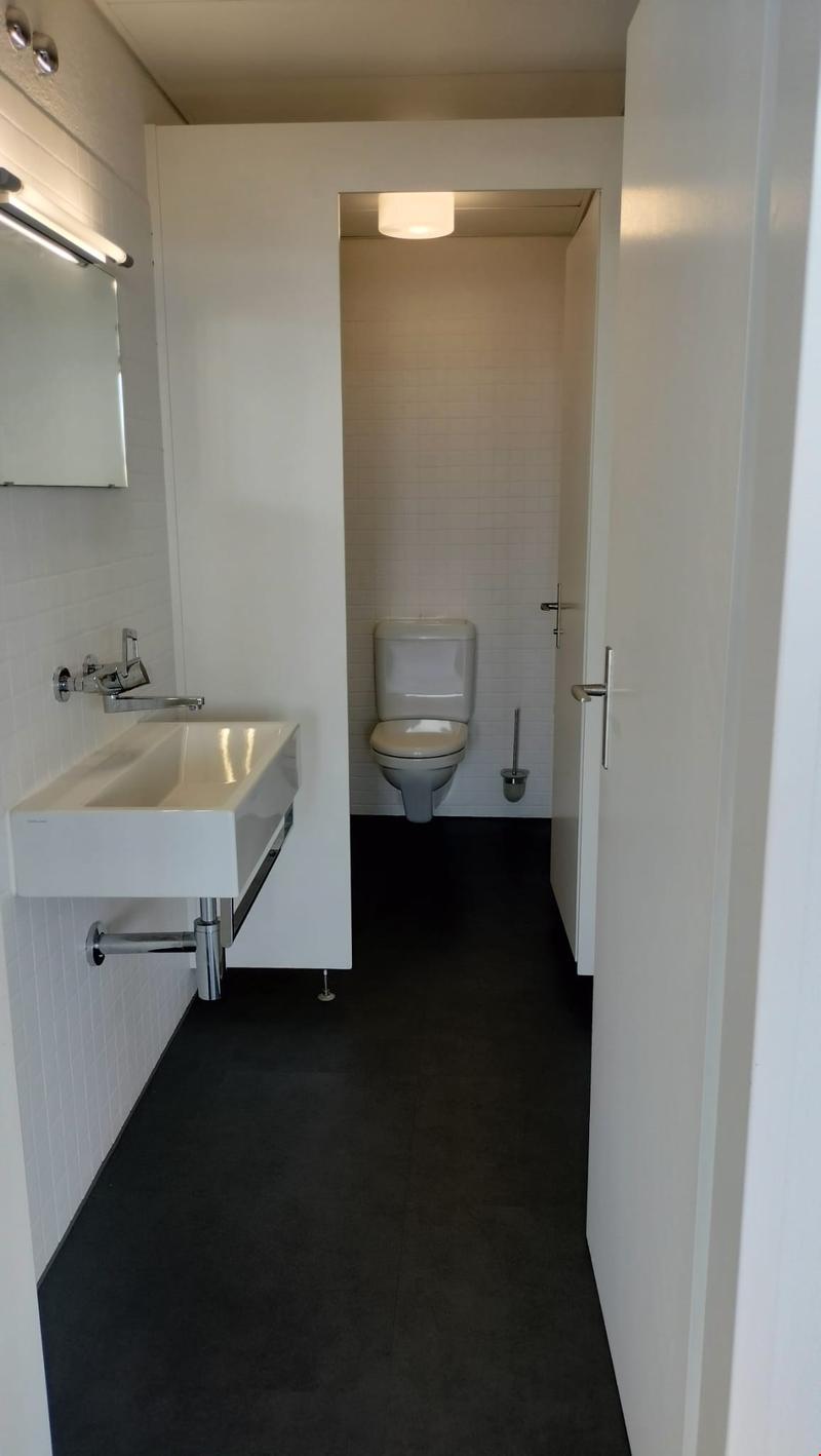Bathroom with white walls, black floor tiles, a vanity sink, and a toilet. The room also has a private washing machine.