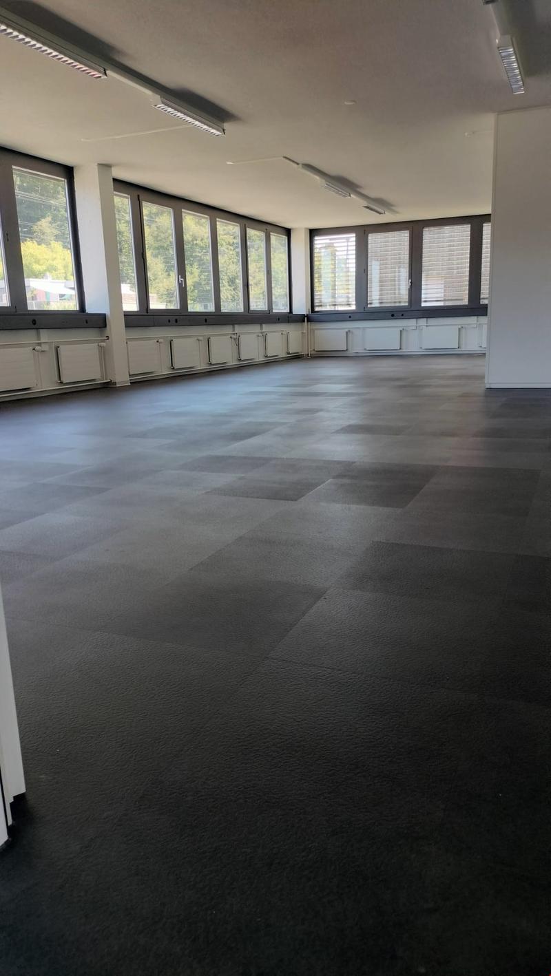 Large open room with floor-to-ceiling windows, grey tiled flooring, and minimal furnishings