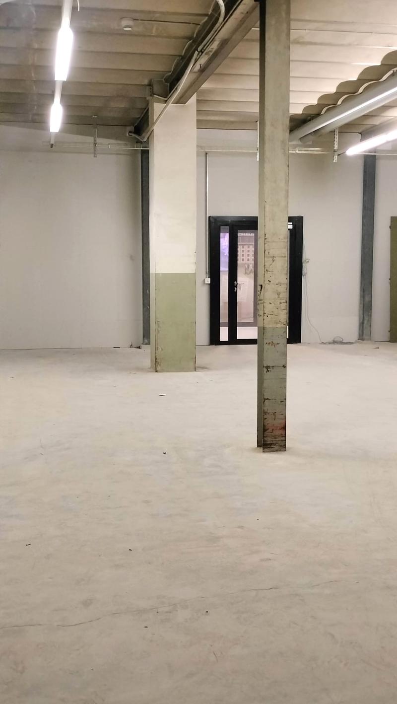 Empty room with white walls, exposed concrete columns, industrial lighting, doorways, and power outlets.