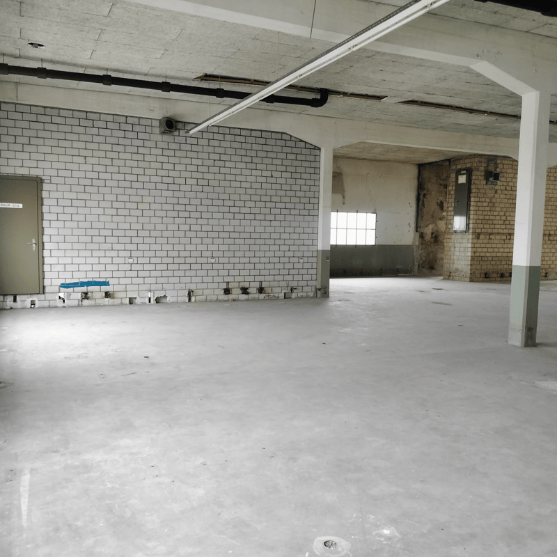Concrete floor, white tiled wall, exposed brick wall, concrete support beam, electrical conduit, open doorway