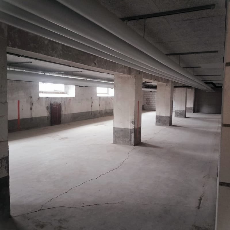 large open space, concrete floor, exposed ceiling beams, concrete columns, bare concrete walls, two small windows, one door