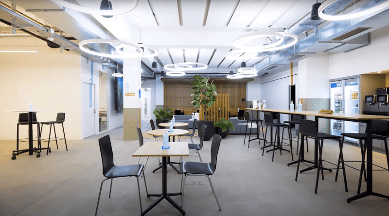 Empty cafeteria, several tables, chairs, plants, tables with bottles, refrigerator