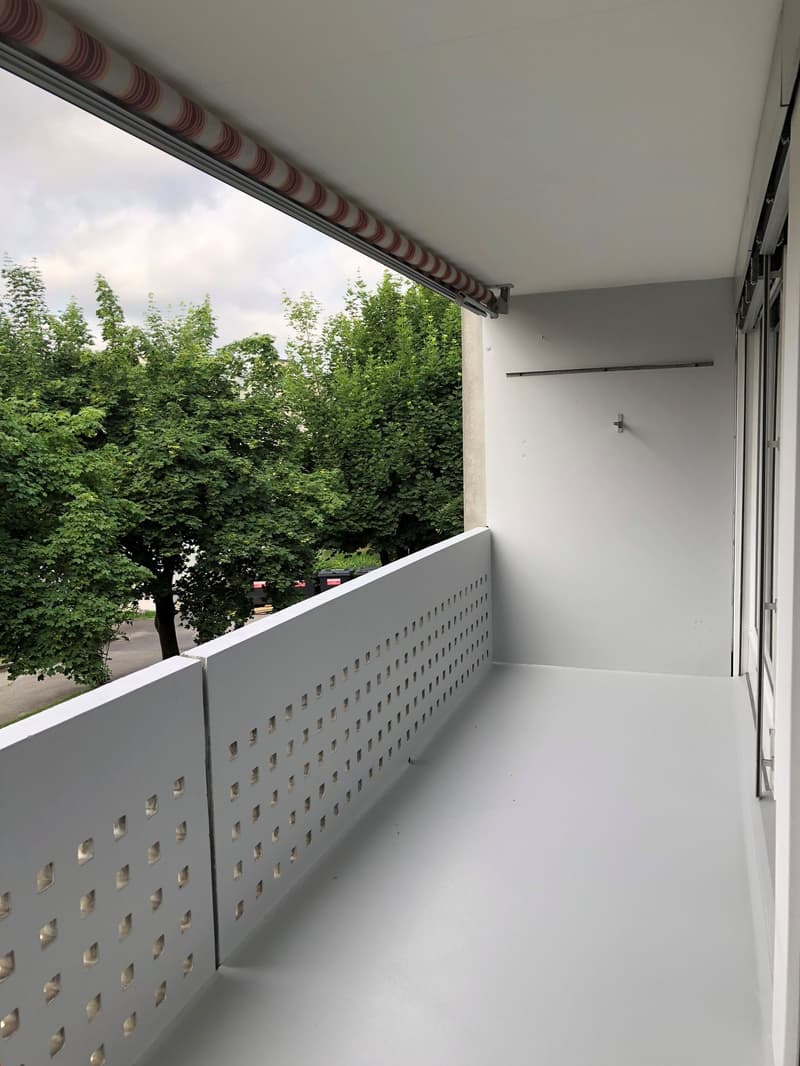 Balcony with white railing, white floor, white walls, trees outside