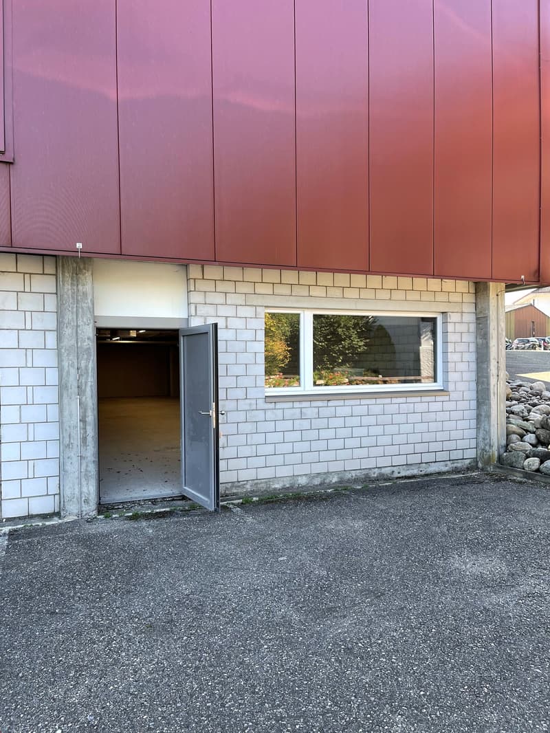 Red exterior wall, white tiled wall, concrete pillars, open door, garage, road, parked cars