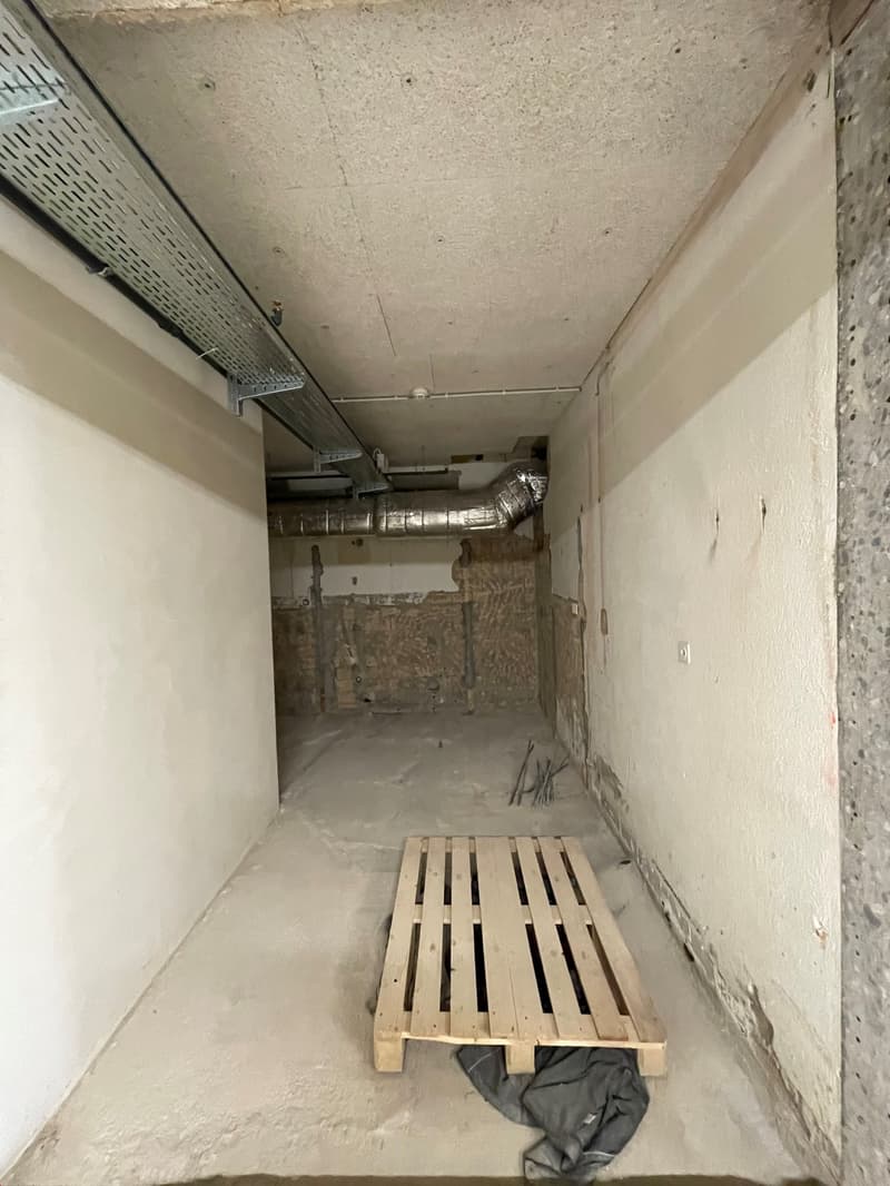 Empty room with white walls and ceiling, grey concrete floor, metal pipe on ceiling, wooden pallet, wire on floor