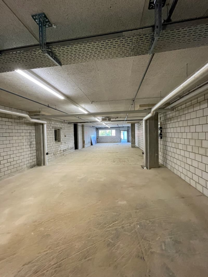 Empty basement with white brick walls, exposed concrete floor, metal ceiling beams, and exposed pipes.