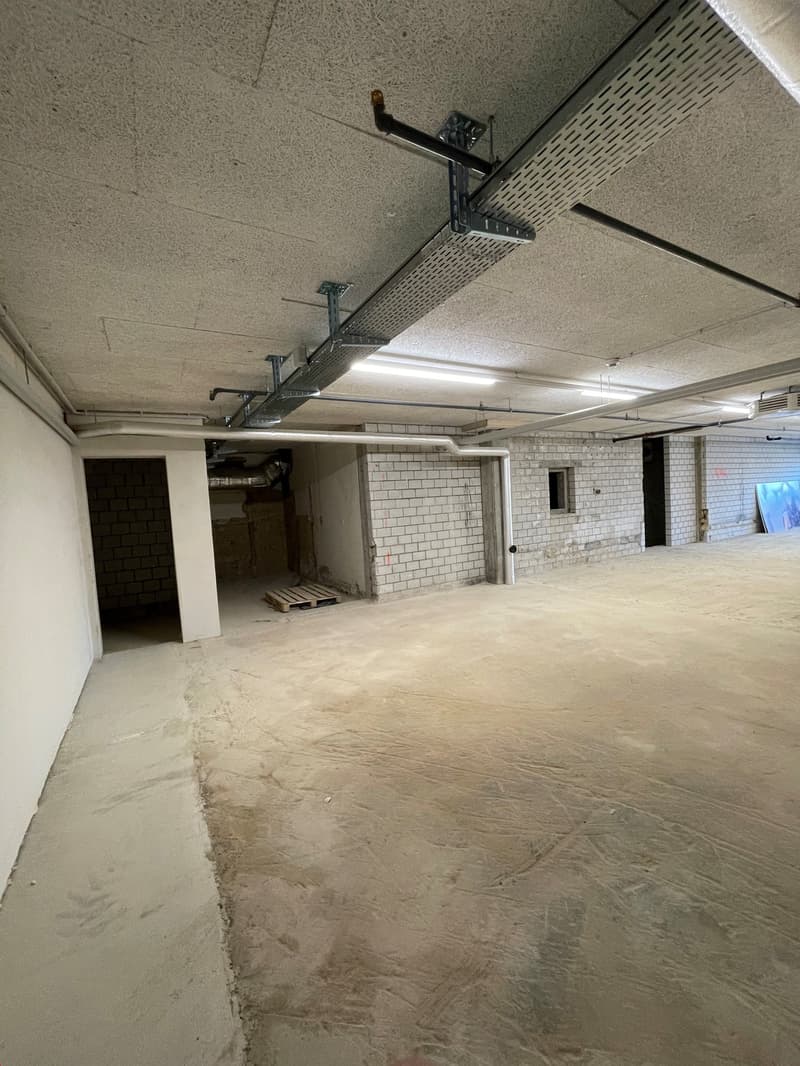 Empty basement, bare concrete floors, white brick walls, exposed pipes, metal ducts on ceiling, no visible features