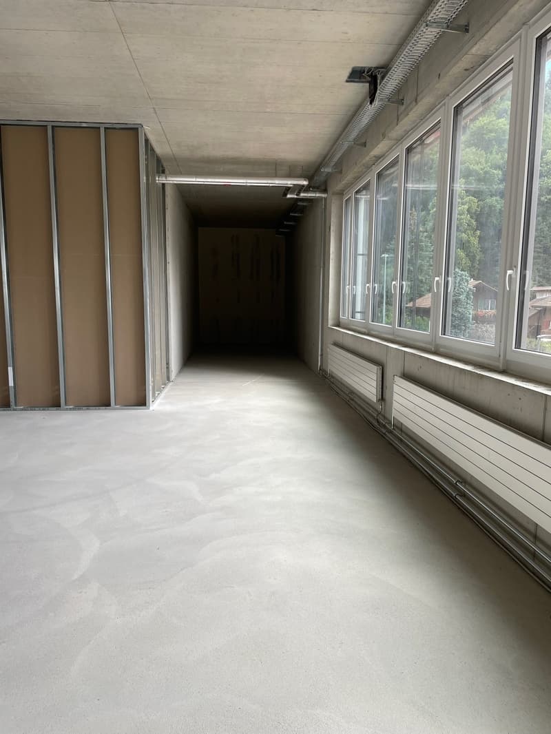 Corridor with concrete floor, windows, unfinished walls, heating pipes