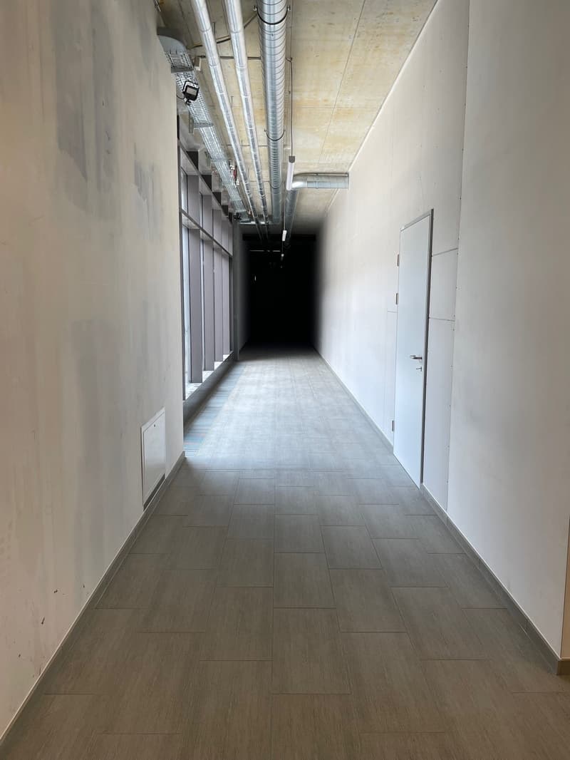 Empty hallway, white walls, tiled floor, ceiling with ducts, a closed door on the right side.