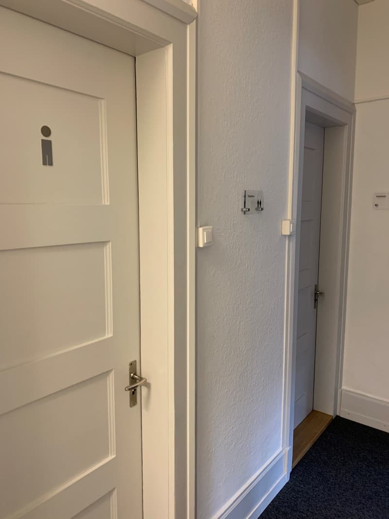 Two doors, white walls, a door knob, a sign above the door, two switches on the wall