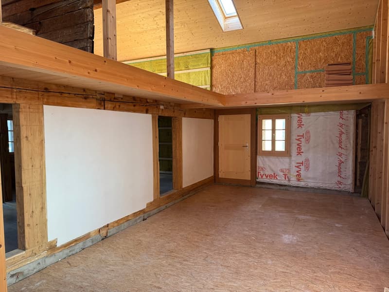 Unfinished interior space with exposed wooden beams, insulation, and drywall. The room appears to be in the process of construction or renovation, with a window and a door visible.