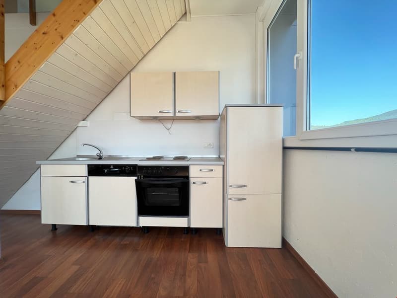 Compact kitchen with white cabinets, stove, oven, and refrigerator. Hardwood flooring and large window providing natural light.
