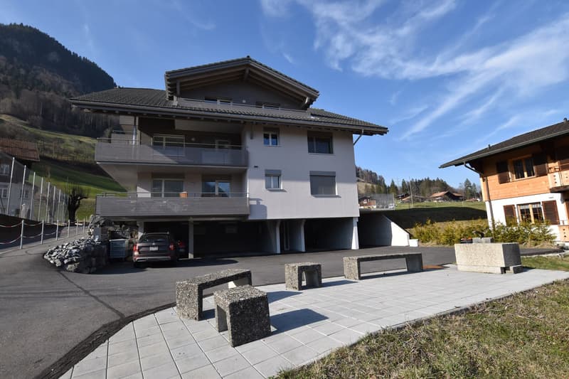 3 story building, grey, underground garage, multiple balconies, mountain view, car in the driveway