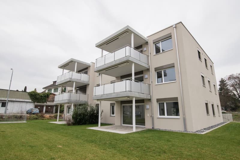3 story apartment building, beige exterior, multiple balconies, glass doors, green lawn