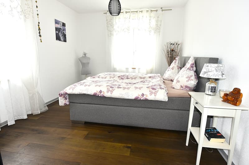 white walls, wooden floor, double bed, gray bed frame, white pillows, night table, lamp, painting