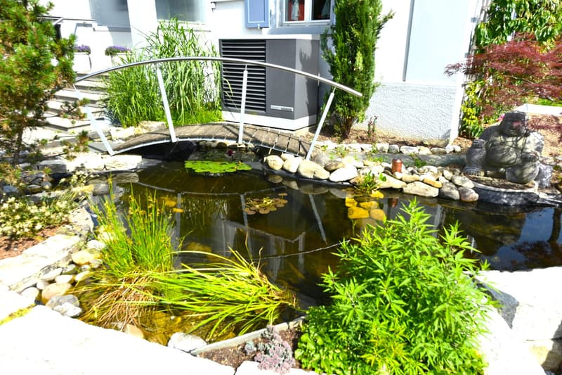 garden with pond, wooden bridge, rocks, plants, and Buddha statue