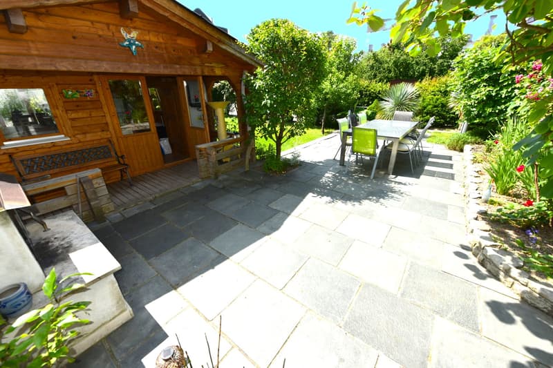 Wooden house with stone floor patio, garden, table and chairs, wooden bench