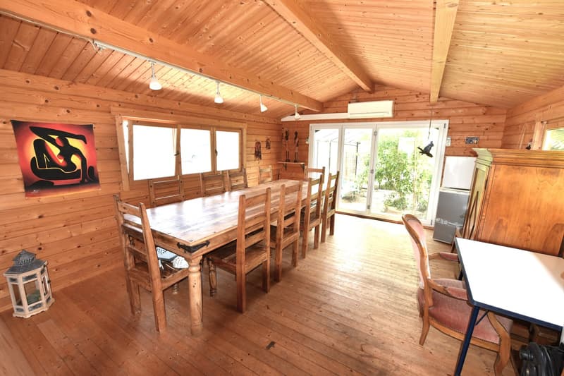 A dining room with wooden walls, floor and furniture, large wooden dining table, chairs, lantern, art piece, sliding glass door, small table and chair, AC unit, table, side table