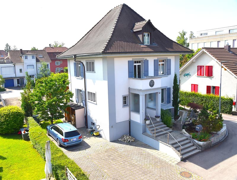 2 story house, white exterior, brown roof, blue windows, grey door, blue garage door, paved driveway, garden, lawn, hedge, mailbox, stairs, blue car parked