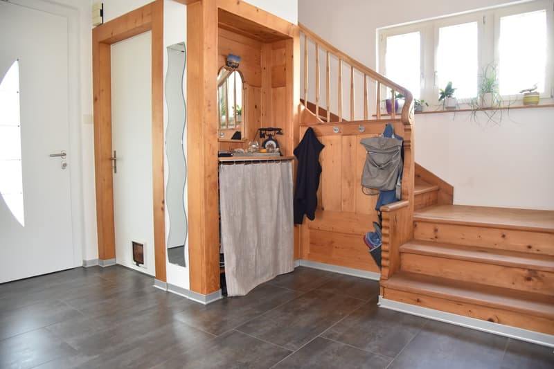 Entrance hallway with wooden staircase, tiled floor, cat door, coat hooks, a shelf with a mirror