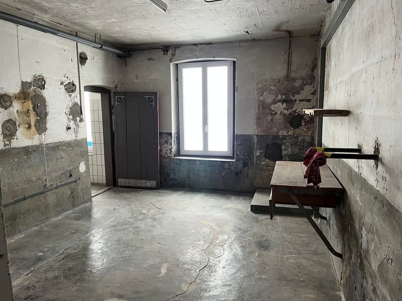 Concrete floor, two doors, a window, a wooden desk against a wall with a metal bracket, damaged walls, pipe