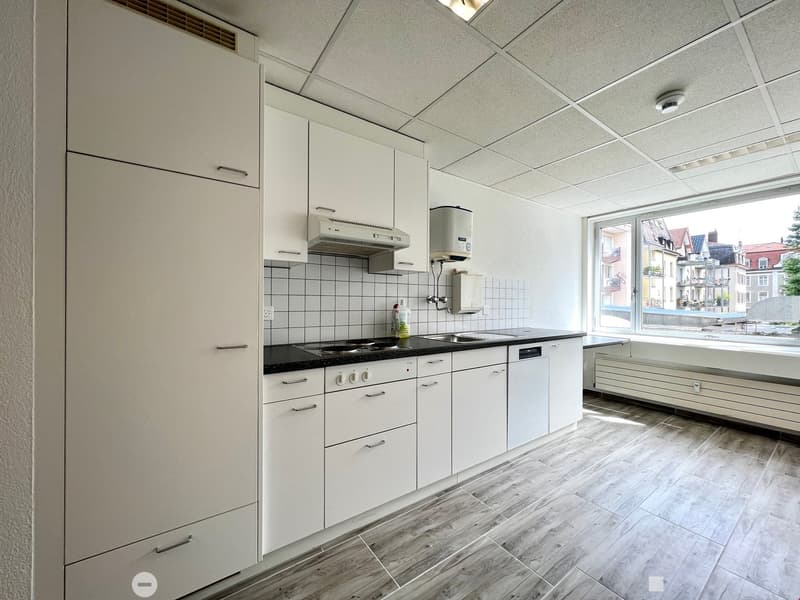 Open concept kitchen, white cabinets, tile backsplash, modern appliances, wooden floor, large window with city view