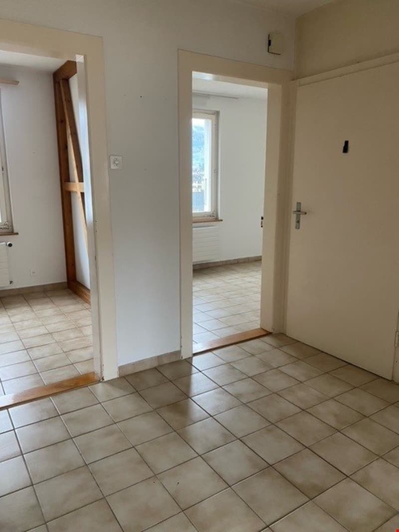 Empty room with tiled floor, white walls, two doors, and a window with a view outside